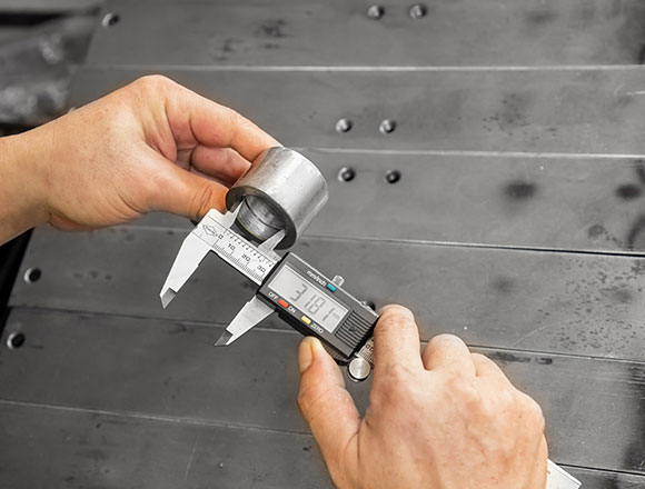 A worker is inspecting steel parts with a calipers