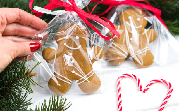 Женская рука держит упакованного пряничного человечка на белом деревянном фоне